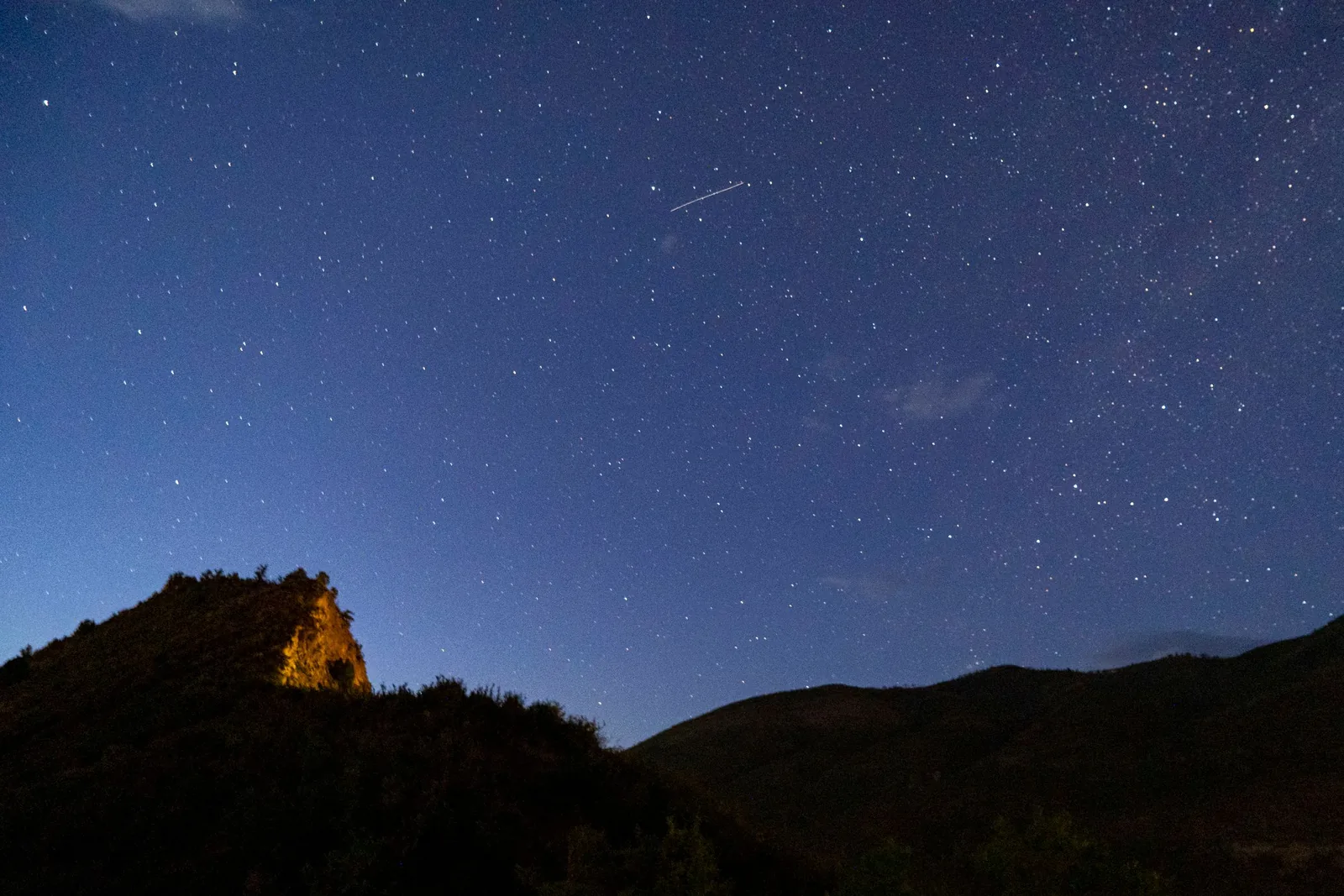 A meteor streaking across a starry sky above mountains